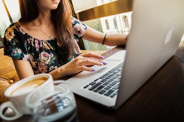 How To Sell My Photos Online - image of a girl working at her laptop with a cup of coffee in the foreground